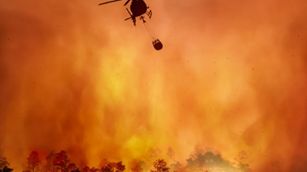A helicopter flying over a forest filled with fire