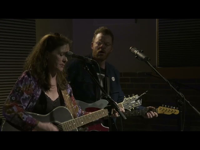 A man and a woman playing guitars in a recording studio