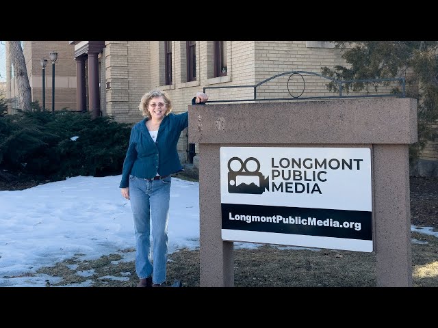 a woman standing in front of a Longmont Public Media sign