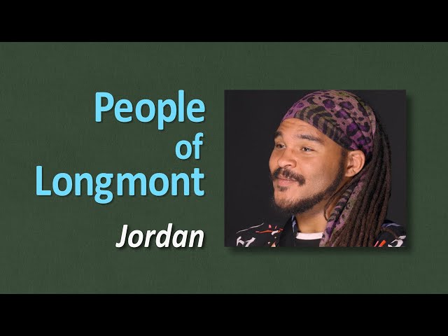 A man with dreadlocks posing next to a sign that reads "People of Longmont Jordan